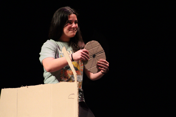 Student during March Madness performance driving a prop car across stage.